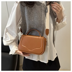 Close-up of brown leather crossbody bag with curved flap and white canvas shoulder strap
