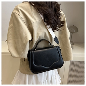 Detail of minimalist black leather saddle bag with wide white fabric shoulder strap