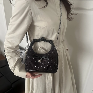 Elegant black rivet handbag with bow and pearl detail shown on model with chain strap