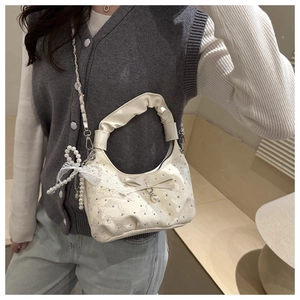 Dettaglio borsa a tracolla in pizzo floreale con catena di perle e fiocco decorativo