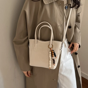 Borsa a secchiello beige minimalista con ciondolo in perline su un trench coat kaki