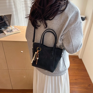 Foto lifestyle di una borsa tote nera con ciondolo in legno indossata a tracolla