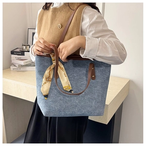 Detail of denim tote bag with brown leather handles and decorative silk scarf detail
