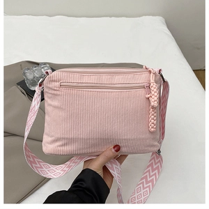 Detail of pink corduroy crossbody bag with woven shoulder strap and zipper pocket