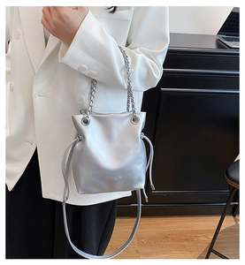 Detailed view of a silver bucket bag featuring metal chain and drawstring on white blazer