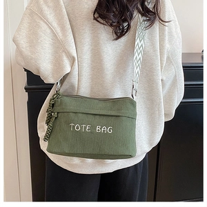 Model wearing a green corduroy tote bag with embroidered letters and woven shoulder strap