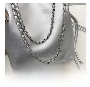Detail view of the silver metallic bucket bag featuring the woven chain and textured logo