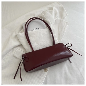 Close-up of a burgundy underarm bag with decorative side bows and a glossy finish