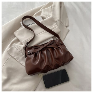 Close-up of brown pleated shoulder bag with bow detail and silver star studs on a blazer