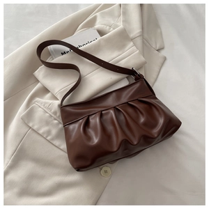 Detailed view of dark brown pleated hobo bag with sleek finish on a blazer background