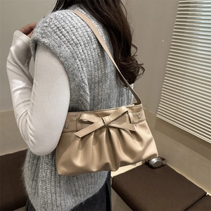 Elegant beige bow shoulder bag with pleats and star rivets shown on a female model