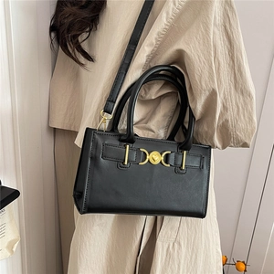 Black leather handbag with golden heart buckle, styled with a beige trench coat