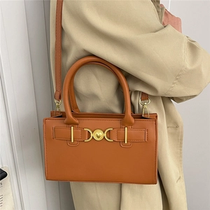 Caramel brown leather crossbody bag with golden heart clasp shown on a beige coat