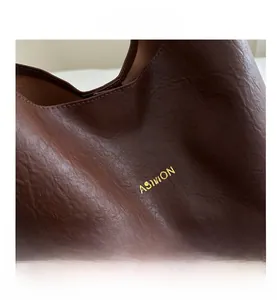 Detailopname van donkerbruin generfd leer en het gouden Fashion logo op de tas