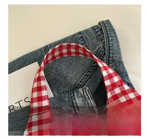 Détail de la poignée large et confortable sur un sac fourre-tout en toile à carreaux rouge