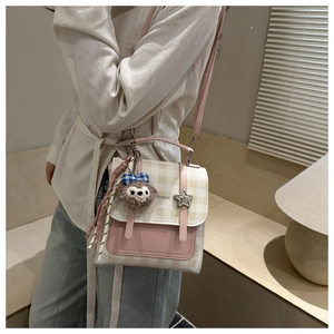 Detail of pink plaid crossbody bag featuring silver star buckle and plush bear charm