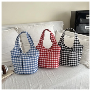 Détail de trois sacs cabas en toile à carreaux bleu rouge et noir sur un canapé