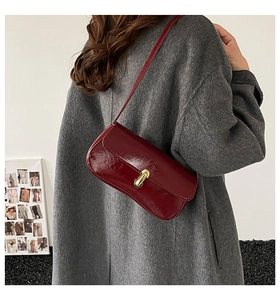 Close-up of deep red baguette shoulder bag with golden buckle on model wearing wool coat