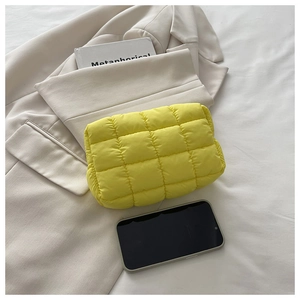 Macro shot of bright yellow quilted nylon clutch bag on a beige blazer background