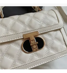 Detail of ivory quilted crossbody bag featuring a modern gold T-shaped twist lock buckle