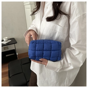 Close-up of blue quilted square vanity bag held by a model in a minimalist modern setting