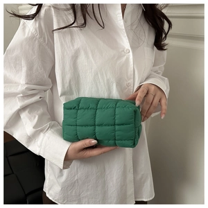 Detail view of a vibrant green quilted makeup bag held by a person in a white shirt