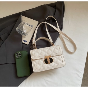 Close-up of a white quilted crossbody bag with a distinctive golden T-bar metal lock