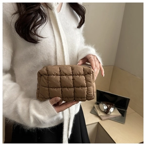 Detail view of khaki quilted down cosmetic bag held by a model in a cozy setting