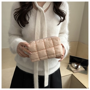 Quilted peach pink cosmetic bag with soft texture and metallic zipper detail held by model
