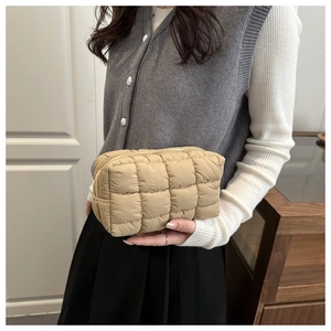 Detail view of khaki quilted puffer nylon cosmetic bag held by a model in daily use