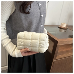 Detail of white quilted puffer clutch with metal zipper held in a cozy cafe setting