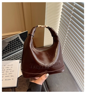 Detail of dark brown dumpling bag with Maison embossing and gold hardware in natural light