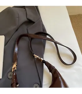 Close-up of adjustable strap with gold buckle on a dark brown patent leather bag