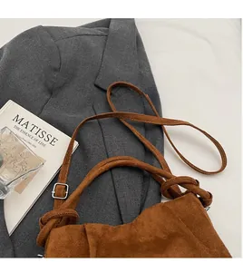 Close-up of brown suede handbag with top knot detail against a grey blazer background