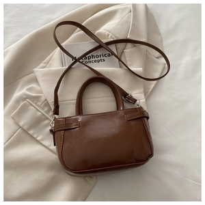 Détail d'un sac à main marron en cuir PU posé sur un blazer avec des boucles en argent chic