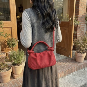Red suede cloud handbag with knot handle and shoulder strap shown in a street setting