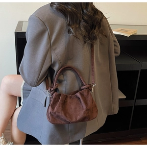Detail of dark brown suede shoulder bag showing pleated texture and round handle on model
