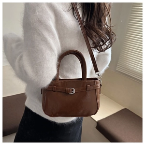 Détail d'un sac à main élégant en similicuir marron foncé porté avec un pull blanc doux