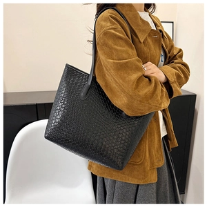 Detail view of black woven leather tote bag with thick texture on shoulder of a model