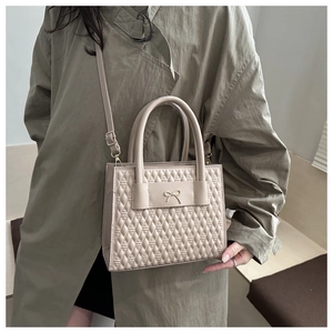 Detail of beige quilted PU crossbody bag with elegant metal bow and cylinder handle