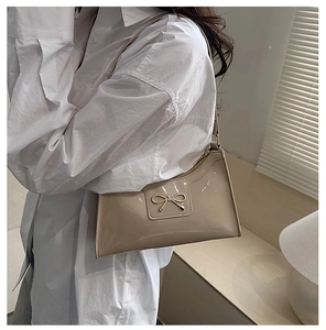 Detail of beige patent leather shoulder bag with a gold metal bow on a model