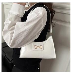 Detail of white patent leather underarm bag with a golden bow buckle on model