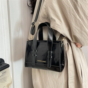 Detail of black glossy handbag with gold logo lettering and adjustable shoulder strap