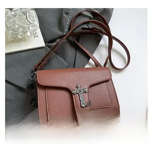 Detail of reddish-brown litchi pattern leather bag with silver gothic cross and strap
