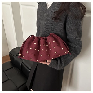 Close-up of burgundy suede cloud bag with gold studs and drawstring closure details