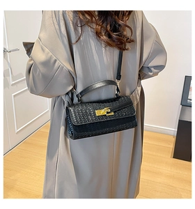Detail van zwarte geweven handtas met gouden draaisluiting op een kaki trenchcoat