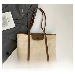 Detailed close-up of canvas tote bag featuring brown leather trim and metal snap closure