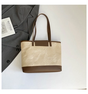 Flat lay of a beige canvas tote with brown leather trim beside a grey blazer and art book