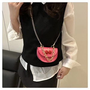 Detailed view of a pink saddle bag featuring red cherry ornaments and a gold chain strap