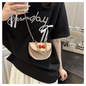 Close-up of beige crossbody bag featuring golden chain and cherry pendant detail